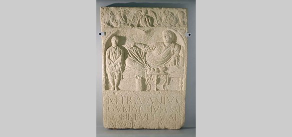 Grafsteen van Marcus Traianus Gumattius uit de toren van de Hervormde Kerk Dodewaard. Afgebeeld een dodenmaal: een man liggend op een bank, voor hem een tafel met eten en drinken, aan zijn voeten een bediende of slaaf.