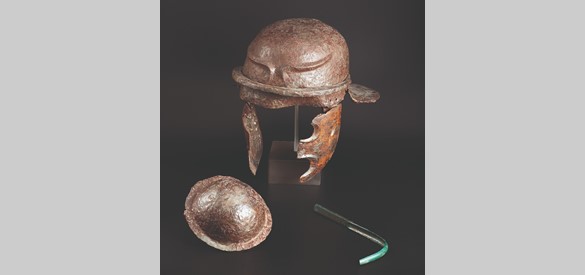 Inhoud van een kuil: ijzeren helm van het type Weisenau, een ijzeren schildknop en een bronzen huidschraper.