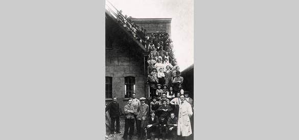 Personeel van schoenfabriek ‘De Ooievaar’ aan de Kerkstraat poseert op de trap van de fabriek in 1925. Onder de arbeiders zijn kinderen die net van de lagere school komen.