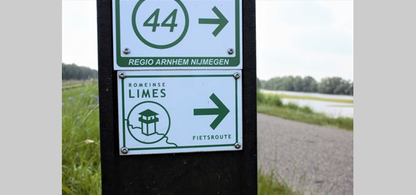 Een wegwijzerpaaltje op de Herwens dijk met daarop een route aanduiding voor de landelijke Romeinse Limes fietsroute.