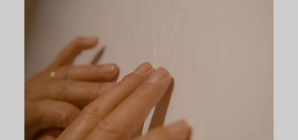 Een detailfoto van twee handen die voelen aan een schilderij