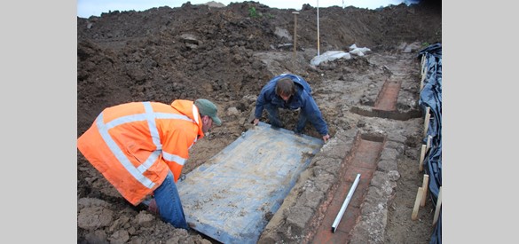 Archeologen halen een stuk goot uit de grond.
