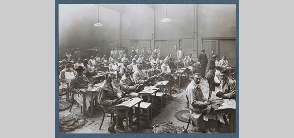 Mannen verwerken tabaksbladeren in een zaal, vermoedelijk in een sigarenfabriek in Nederland, anoniem, 1900-1920