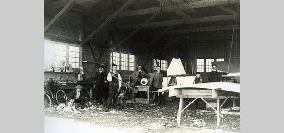 Foto, vliegtuig in aanbouw. Op de voorgrond staat de heer Melgers. Links vooraan zit de vliegenier J.W.E.L. Hilgers, 1910. Collectie Historisch Museum Ede