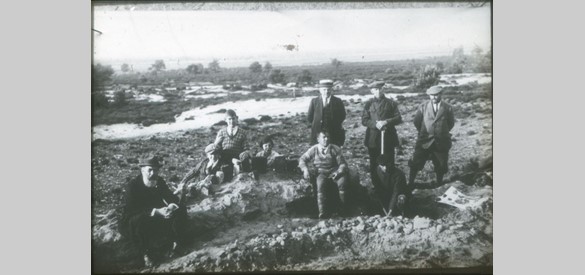 1928. Tijdens de opgravingen op de Ginkelse Heide te Ede o.l.v. kapitein H.J. Bellen. V.l.n.r. notaris W.F.J. Fischer; zoon van kapitein H.J. Bellen; zoon van W.F.J. Fischer; dochter van kapitein H.J. Bellen; H. Staf (rentmeester met strohoed); zittend in de kuil: kapitein H.J. Bellen; naast H. Staf staan boswachter P. Koudijs en W.F.C.H. Graaf Bentinck, heer van Kernhem. De gravers zijn vader en zoon Van Steenbeek (foto: archief Historisch Museum Ede).